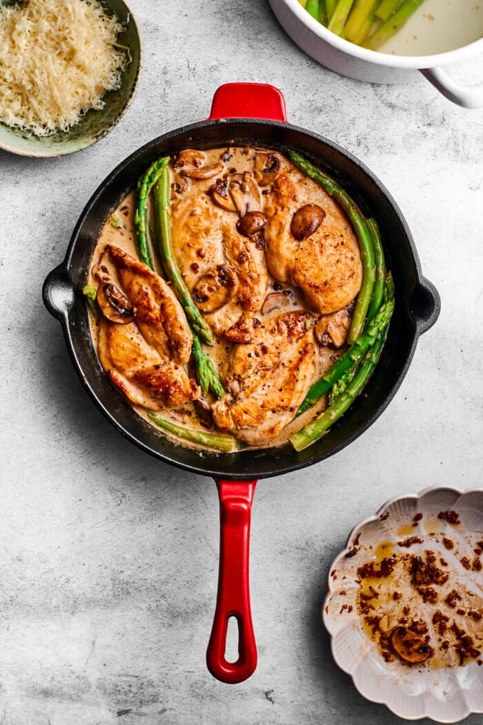 Creamy Chicken Madeira pairs tender chicken breasts with bright asparagus in a rich sauce. Add savory sautéed mushrooms and sweet wine. A finished skillet of chicken madeira rests on a counter.