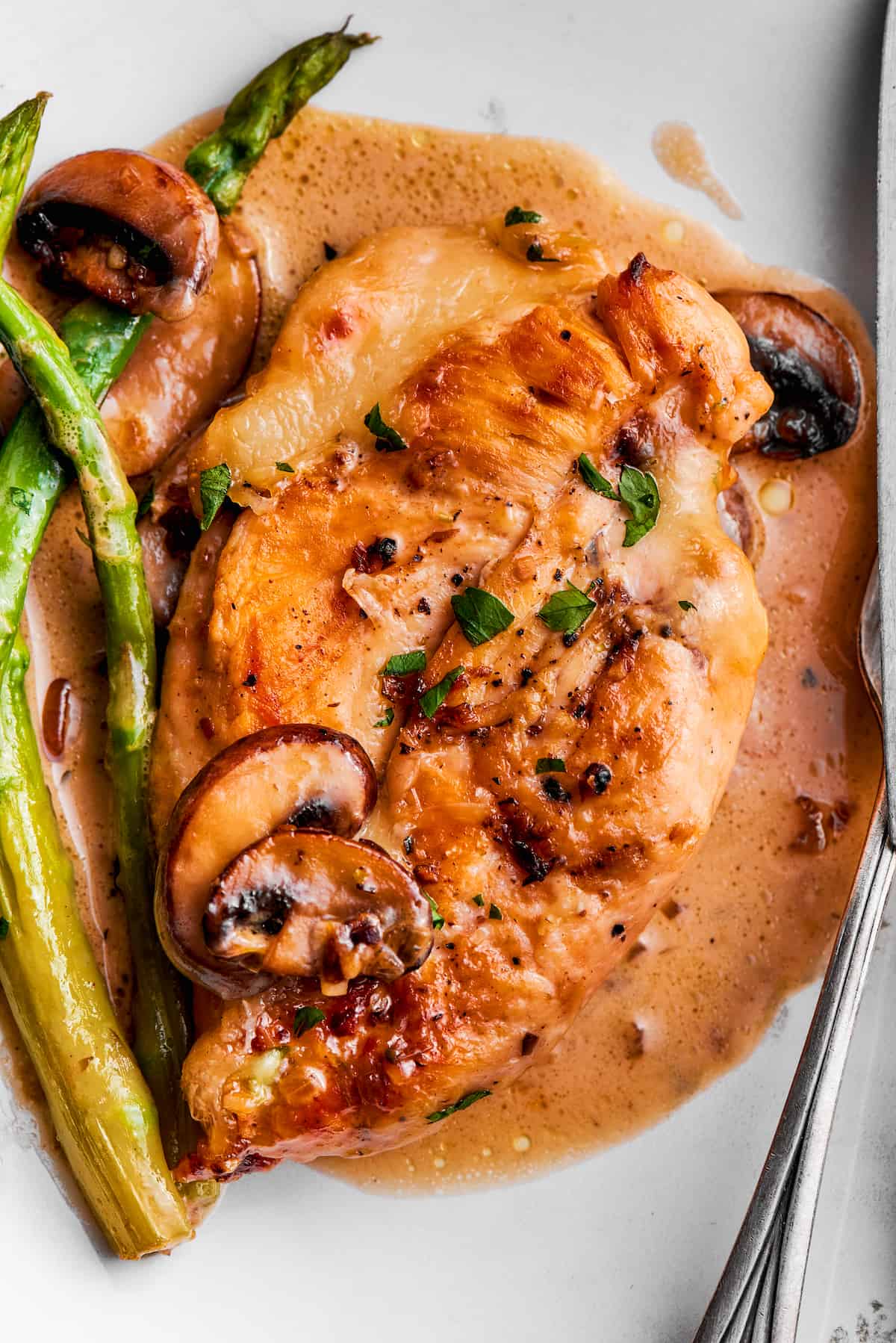 Creamy Chicken Madeira pairs tender chicken breasts with bright asparagus in a rich sauce. Add savory sautéed mushrooms and sweet wine. A plate of chicken madeira shows asparagus and mushrooms on top of it.