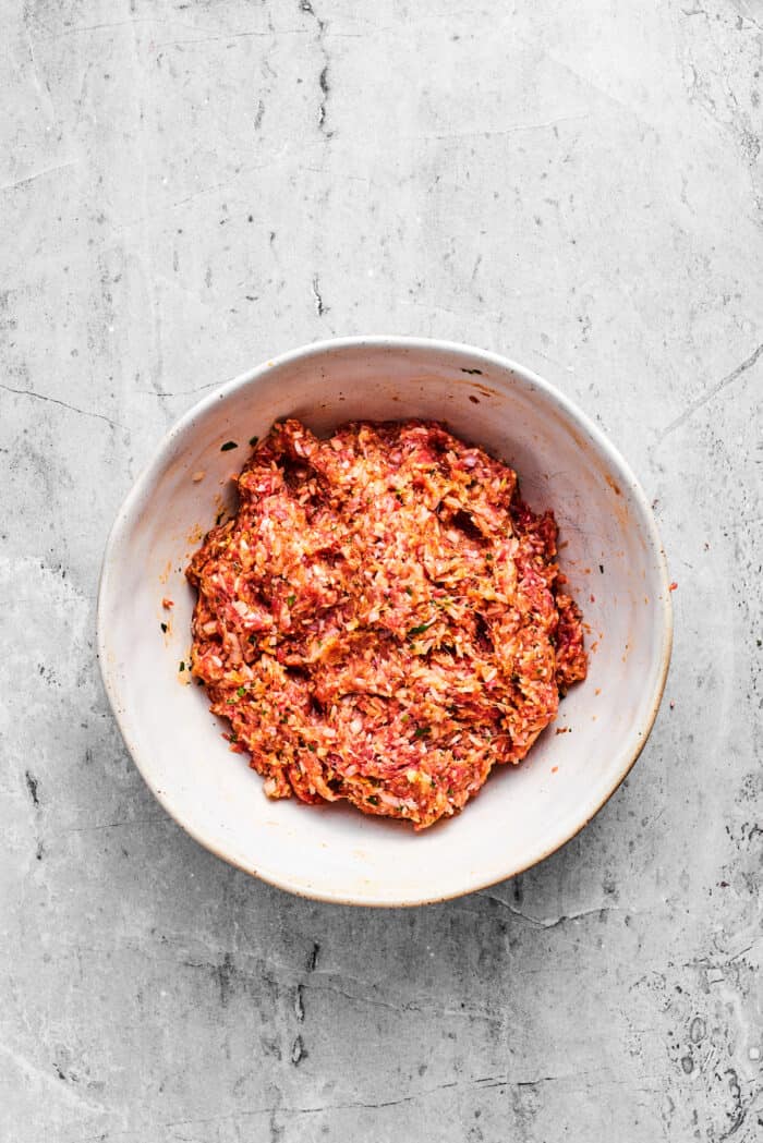 Tender beef and rice Porcupine Meatballs are smothered in tomato sauce to make a savory, filling dish that's perfect with mashed potatoes. The mix for porcupine meatballs in a white bowl.