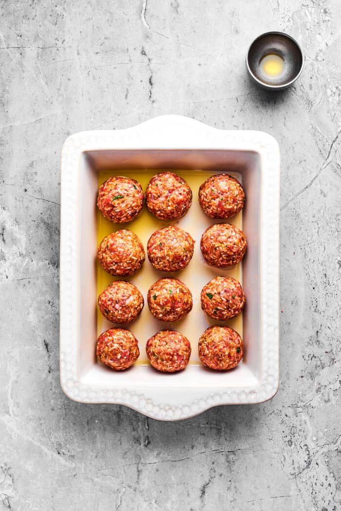 Tender beef and rice Porcupine Meatballs are smothered in tomato sauce to make a savory, filling dish that's perfect with mashed potatoes. A white baking pan holds 12 uncooked porcupine meatballs.