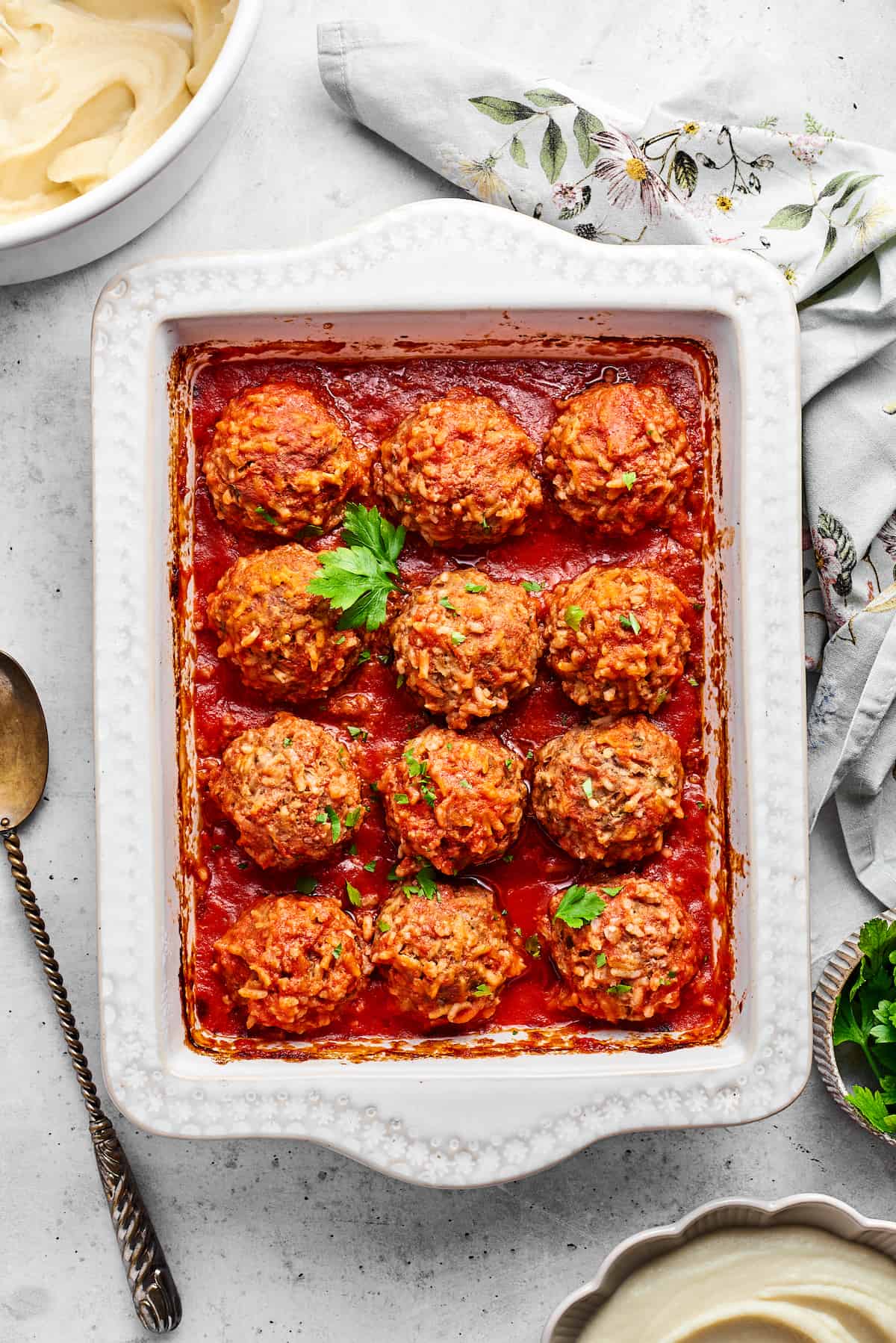 Tender beef and rice Porcupine Meatballs are smothered in tomato sauce to make a savory, filling dish that's perfect with mashed potatoes. A tray of 12 baked porcupine meatballs with a sprig of parsley.