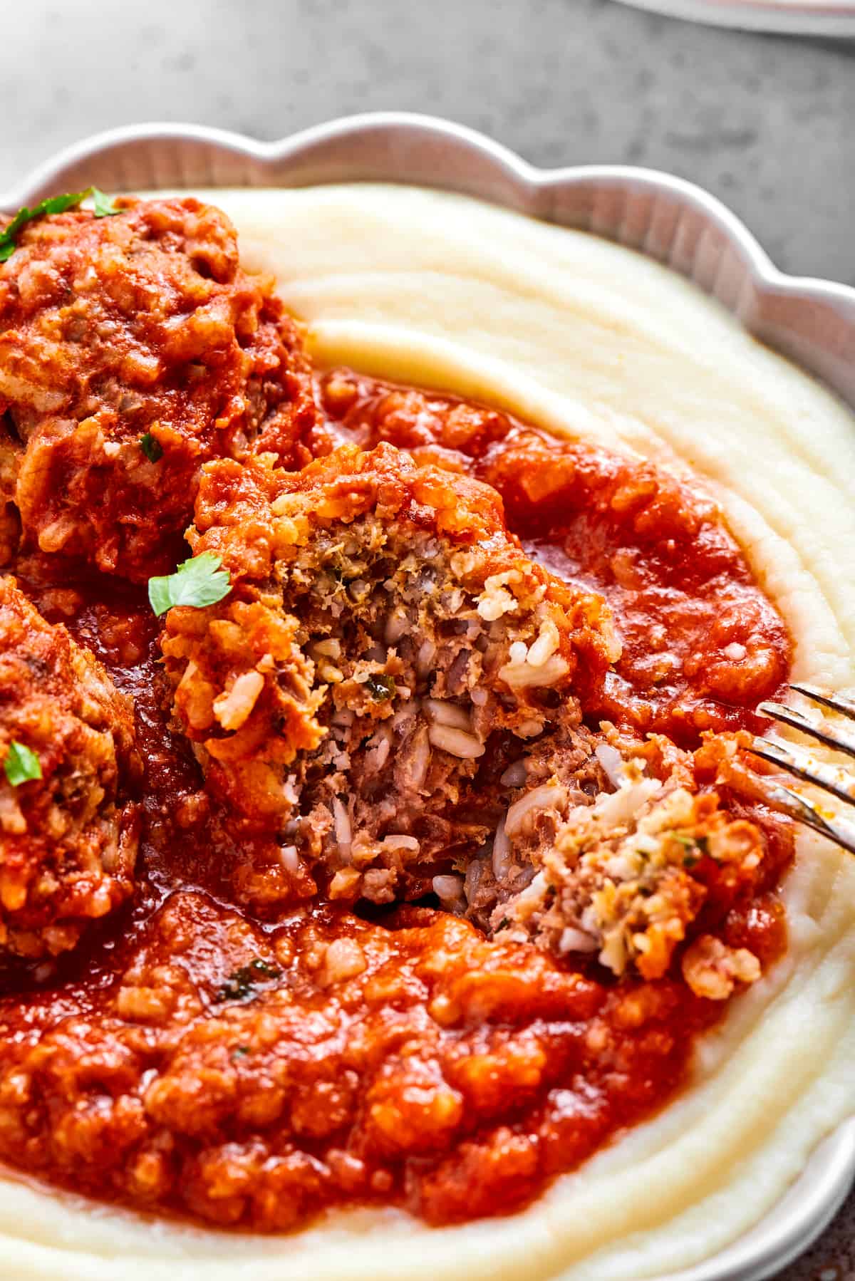 Tender beef and rice Porcupine Meatballs are smothered in tomato sauce to make a savory, filling dish that's perfect with mashed potatoes. A porcupine meatball is cut in half to show its meat and rice interior.