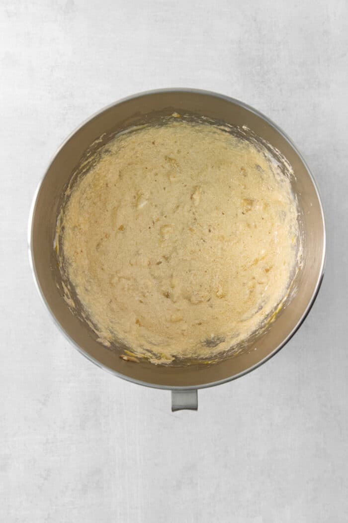 This Banana Coffee Cake features a tender banana bread cake layered with an oat streusel and topped with an optional vanilla bean glaze. The batter for banana coffee cake is mixed in a metal bowl.