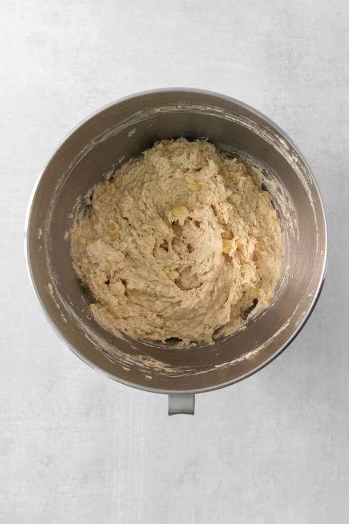 This Banana Coffee Cake features a tender banana bread cake layered with an oat streusel and topped with an optional vanilla bean glaze. Bananas are added to a metal bowl of batter.
