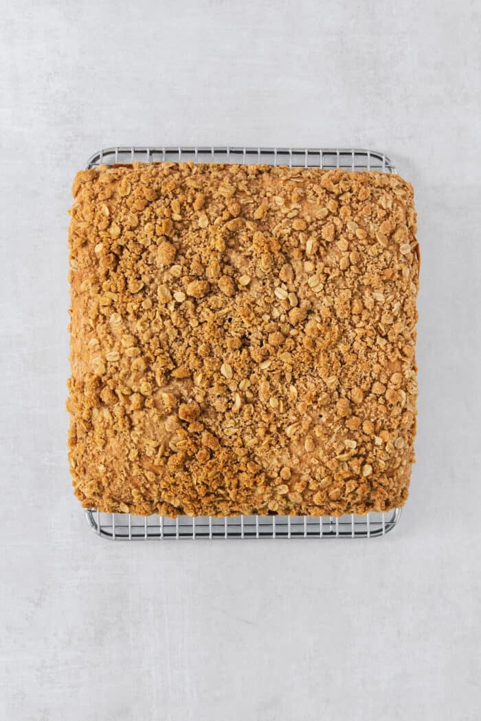 This Banana Coffee Cake features a tender banana bread cake layered with an oat streusel and topped with an optional vanilla bean glaze. A golden, toasted streusel tops a baked pan of banana coffee cake.