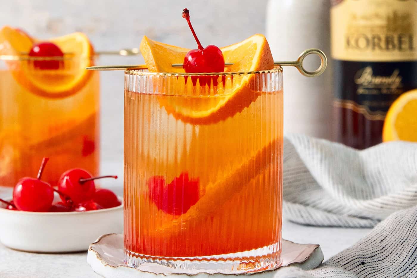 Two glasses of brandy old fashioned are garnish with orange and a cherry.