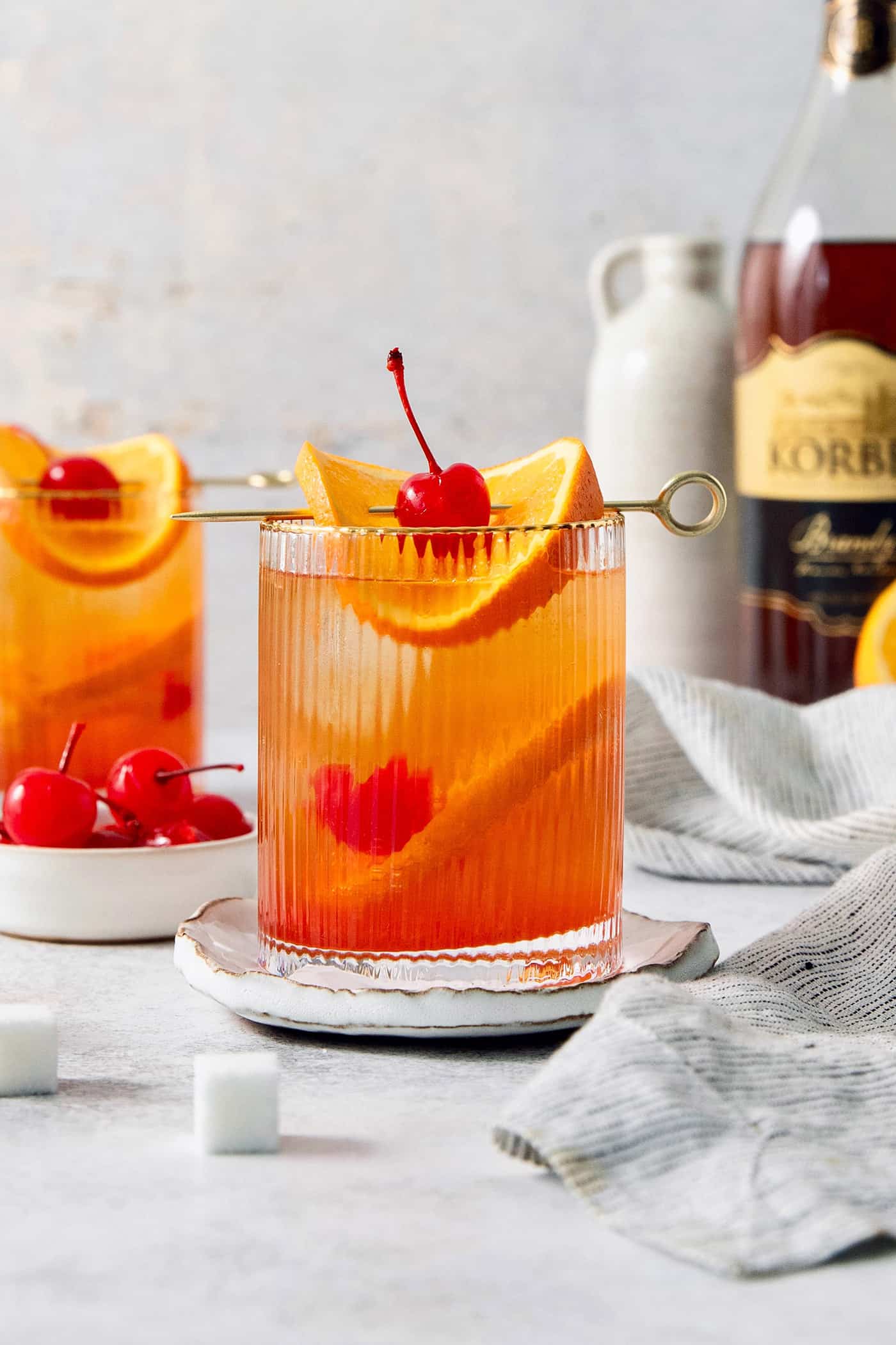 Two glasses of brandy old fashioned are garnish with orange and a cherry.