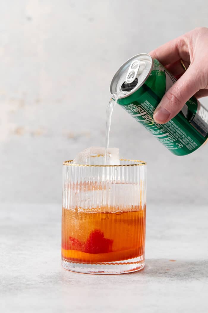 A hand pours 7UP into a glass of brandy old fashioned.