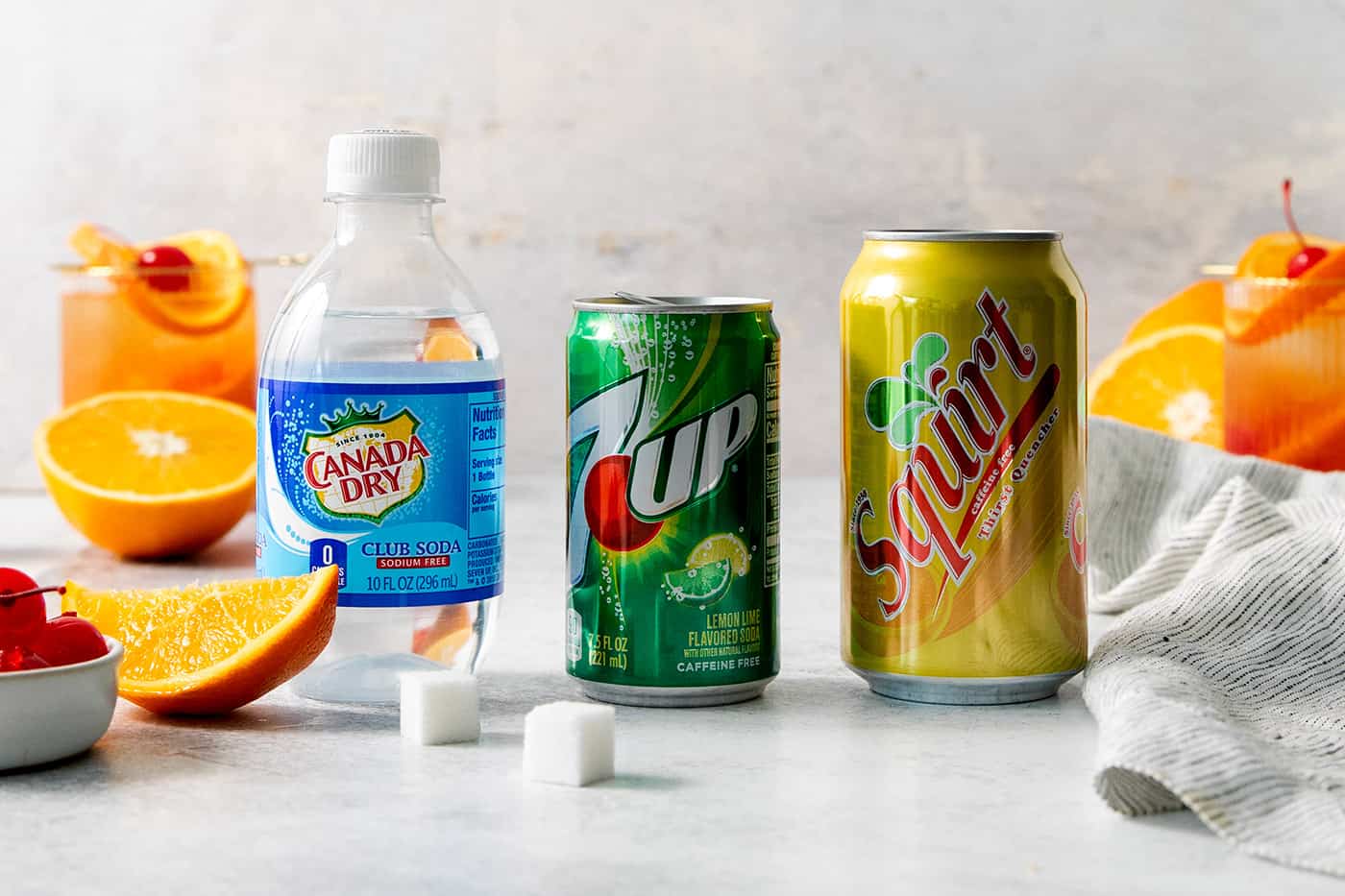 Club soda, 7UP, Squirt, and sugar cubes on a white background.