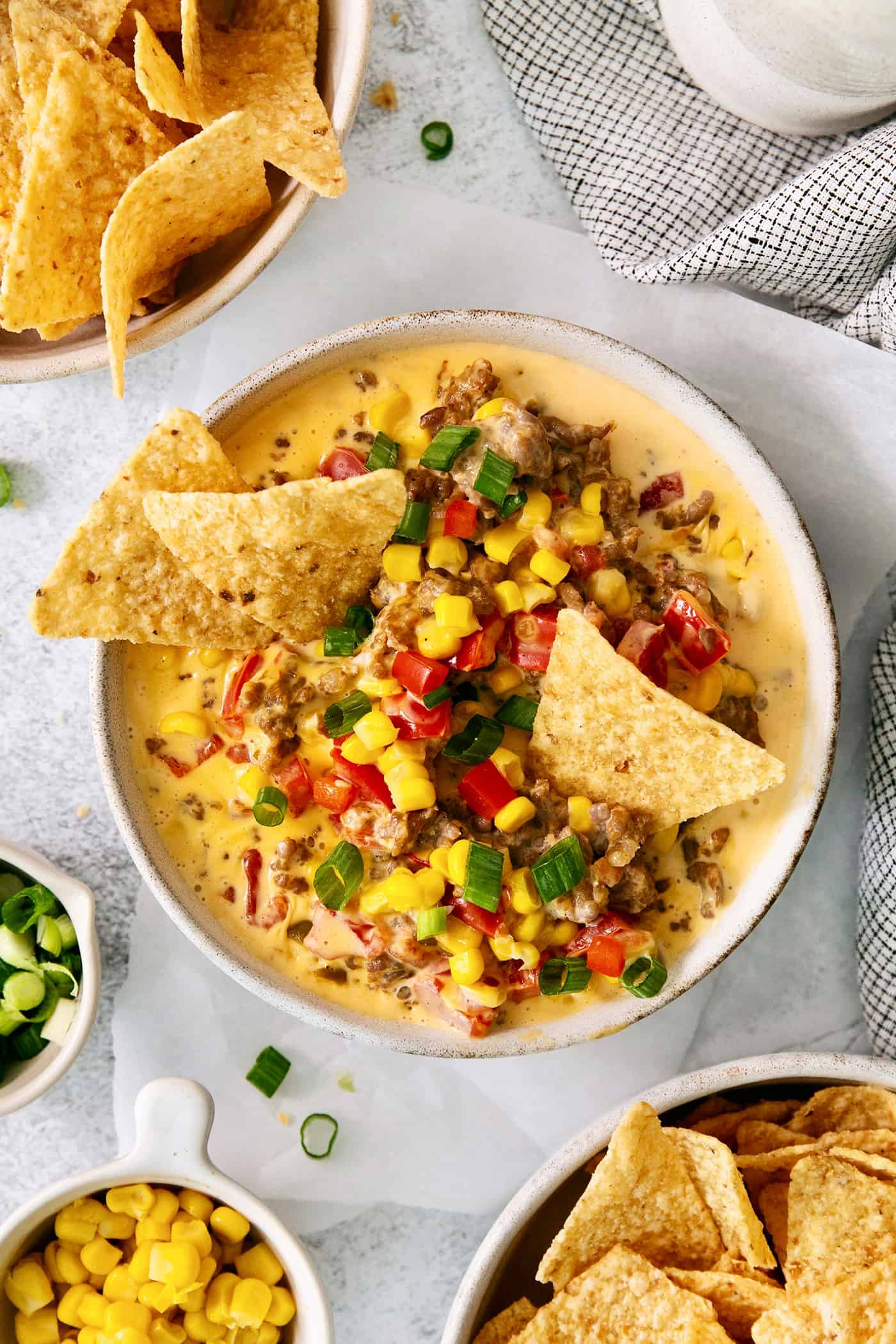 This gorgeously cheesy Sausage Dip takes a creamy base of Velveeta and sour cream and swirls it with spicy sausage and juicy corn kernels. A white bowl of cheesy corn sausage dip is garnished with Rotel and corn chips.
