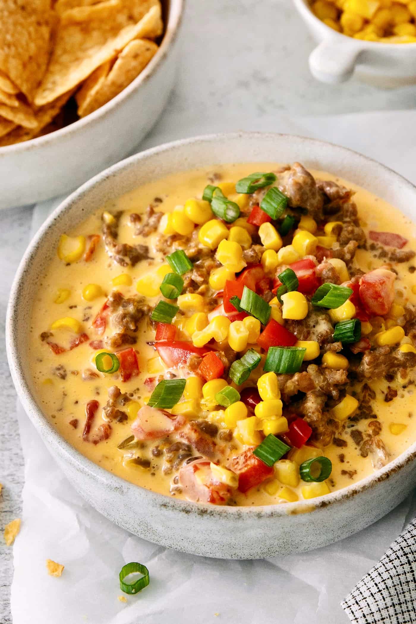 This gorgeously cheesy Sausage Dip takes a creamy base of Velveeta and sour cream and swirls it with spicy sausage and juicy corn kernels. A bowl of cheesy corn sausage dip is topped with corn, tomatoes, and green onions.