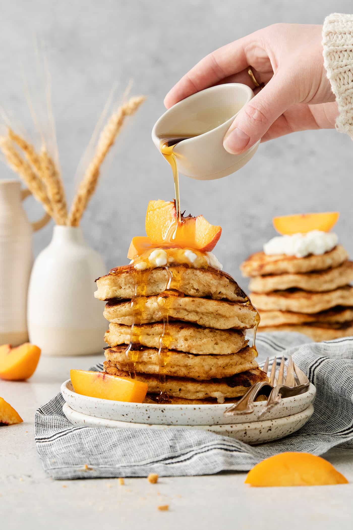 rotein-packed Cottage Cheese Pancakes are light and fluffy, flavored with cinnamon and vanilla, and rich and creamy from cottage cheese. A hand drizzles maple syrup from a small white pitcher over a stack of cottage cheese pancakes.