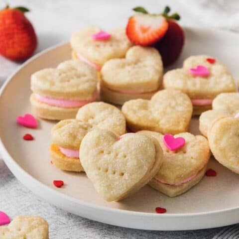 Heart-shaped strawberry cream wafer cookies are displayed on a white plate.