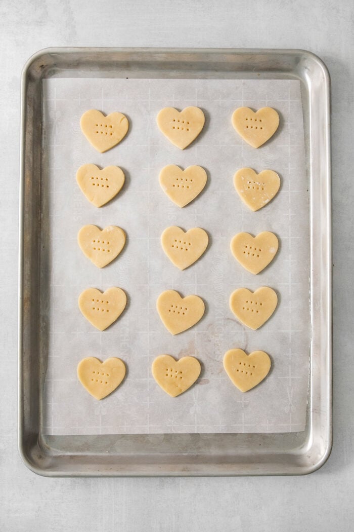 Strawberry Cream Wafer Cookies feature delicate cream and butter cookies that sandwich a pink filling that's fragrant with strawberry extract. Fifteen heart shaped cream wafer cookies are arranged on a cookie sheet.