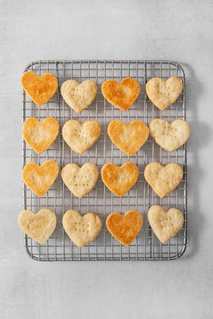Strawberry Cream Wafer Cookies feature delicate cream and butter cookies that sandwich a pink filling that's fragrant with strawberry extract. Baked heart shaped cream wafter cookies cool on a wire rack.