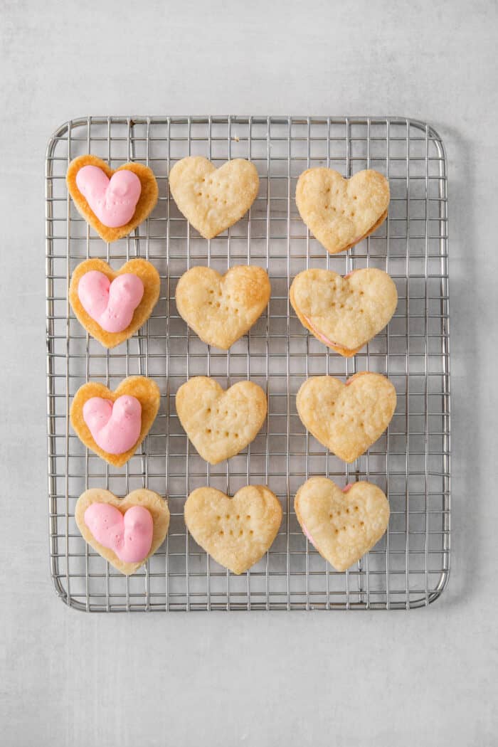 Strawberry Cream Wafer Cookies feature delicate cream and butter cookies that sandwich a pink filling that's fragrant with strawberry extract. Cream wafter cookies, four topped with strawberry buttercream, on a wire rack.