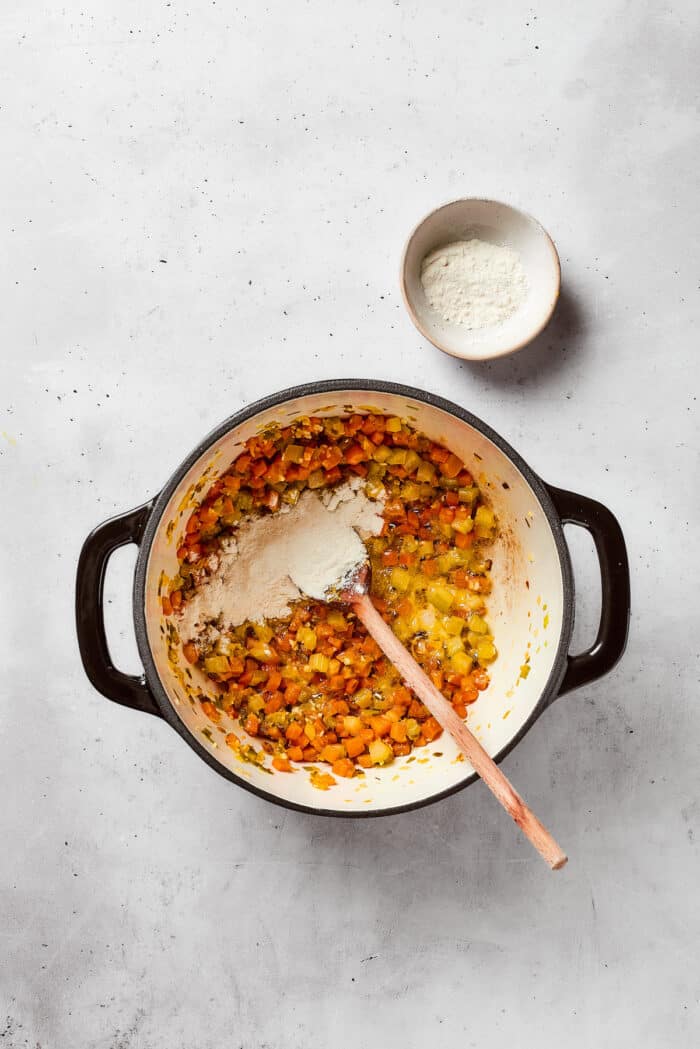 Greek-inspired Lemon Chicken Orzo Soup is fragrant with garlic and packed with tender chicken, vegetables, and delicate orzo pasta. Flour is stirred into a pot of lemon chicken orzo soup.