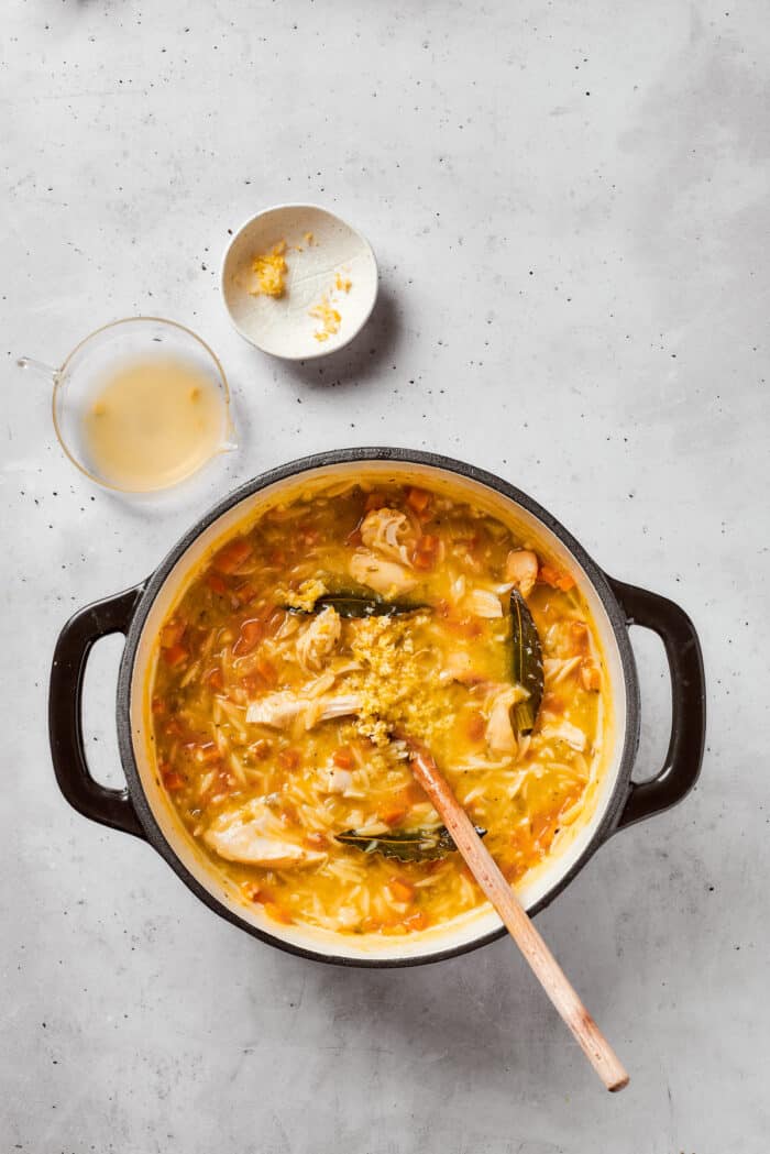 Greek-inspired Lemon Chicken Orzo Soup is fragrant with garlic and packed with tender chicken, vegetables, and delicate orzo pasta. Lemon juice and zest is stirred into a pot of lemon chicken orzo soup.