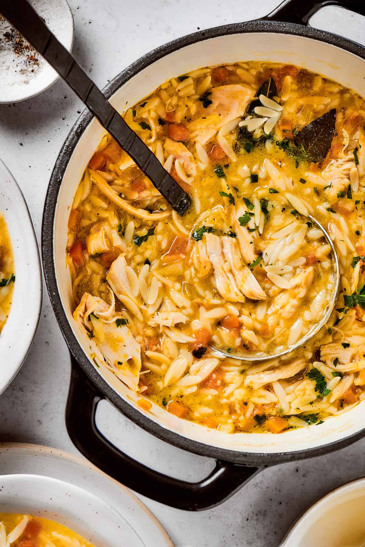 Greek-inspired Lemon Chicken Orzo Soup is fragrant with garlic and packed with tender chicken, vegetables, and delicate orzo pasta. A ladle scoops out a portion of lemon chicken orzo soup from a soup pot.