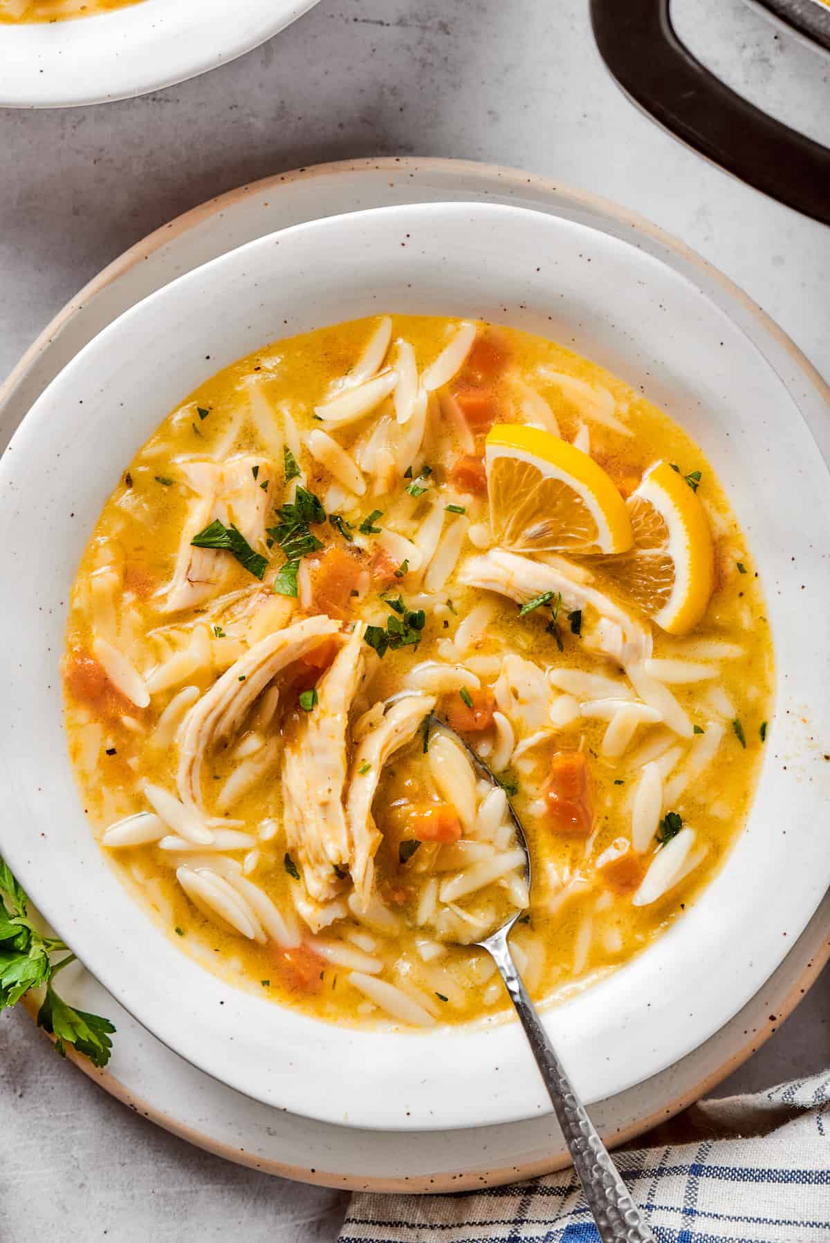 Greek-inspired Lemon Chicken Orzo Soup is fragrant with garlic and packed with tender chicken, vegetables, and delicate orzo pasta. A white bowl brims with lemon chicken orzo soup as a spoon digs in.