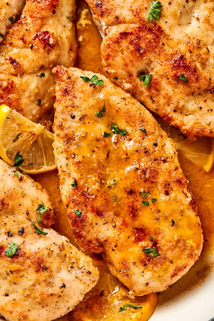 A close up of lemon pepper chicken showing parsley and sauce and browned chicken breast..