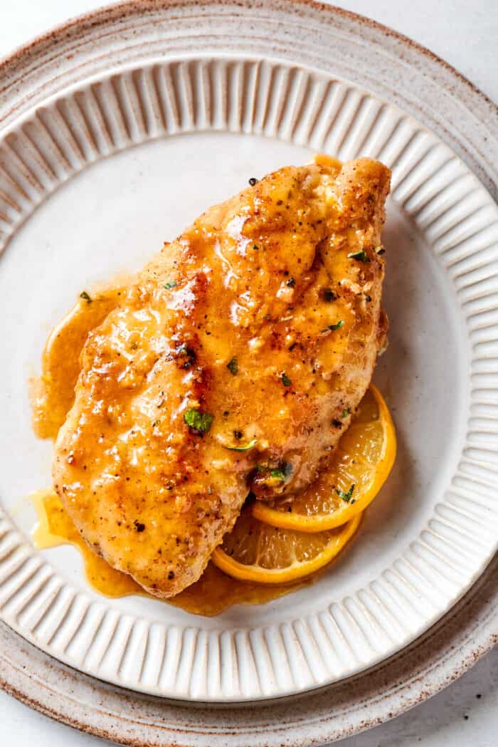 A lemon pepper chicken breast is placed on top of lemon slices on a plate.