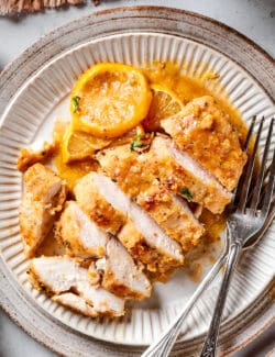 Sliced lemon pepper chicken breast with lemon on a plate.
