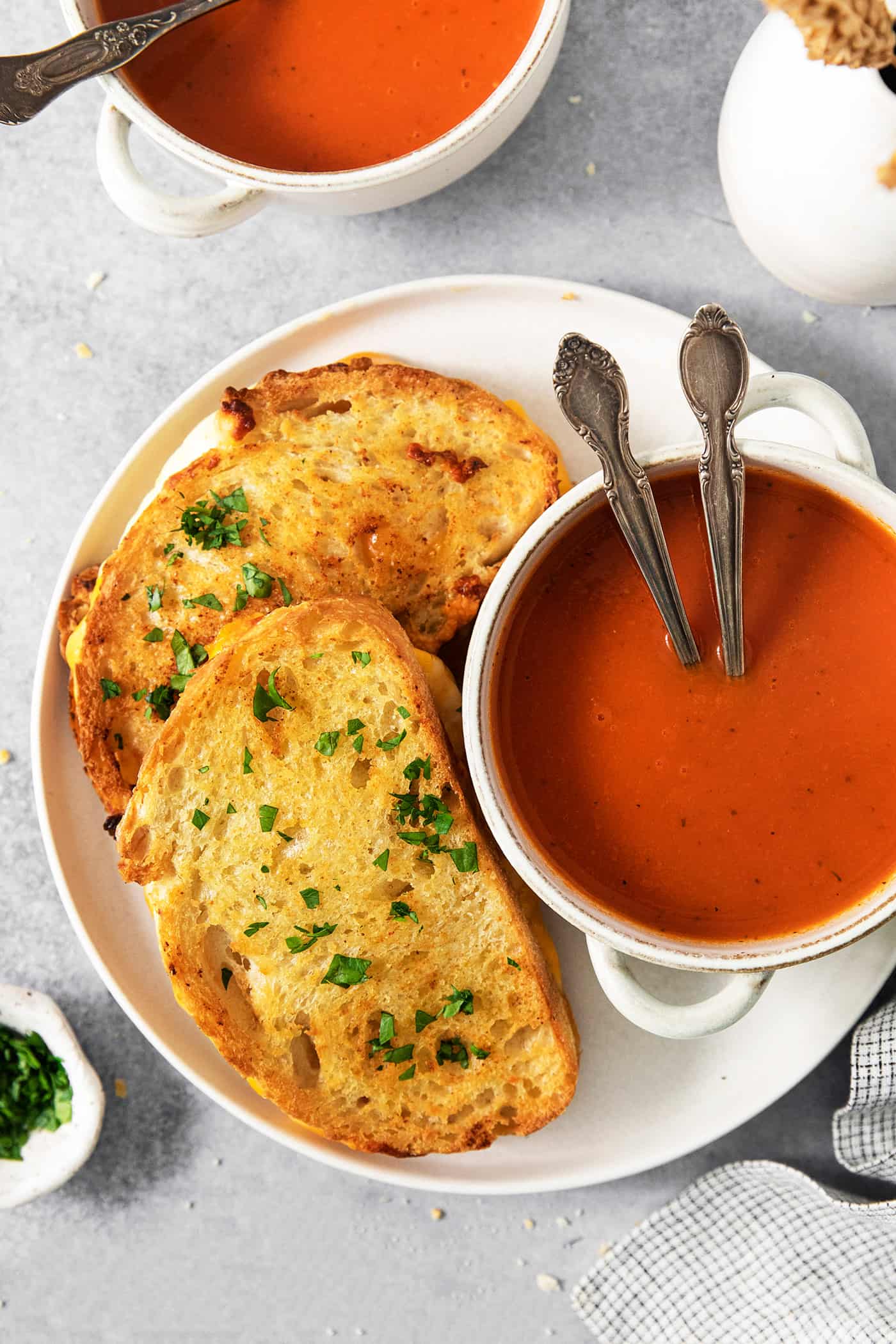Air Fryer Grilled Cheese | Easy Cheesy Grilled Cheese Recipe! A white plate holds a small bowl of tomato soup with two spoons, and two air fryer grilled cheese sandwiches.
