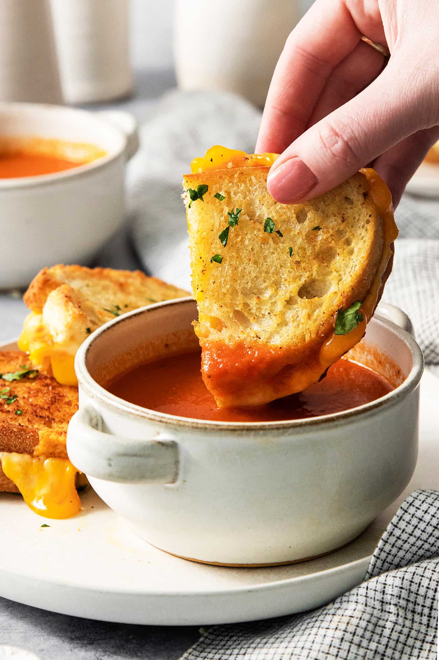 Air Fryer Grilled Cheese | Easy Cheesy Grilled Cheese Recipe! A hand dips a piece of air fryer grilled cheese into a small bowl of tomato soup.