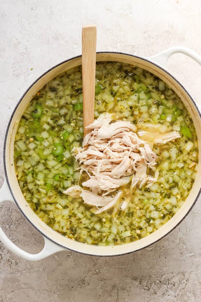This homemade Chicken Noodle Soup is an easy classic with from-scratch chicken broth loaded with tender chicken, vegetables, and egg noodles. A wooden spoon stirs shredded chicken into a pot of chicken noodle soup.