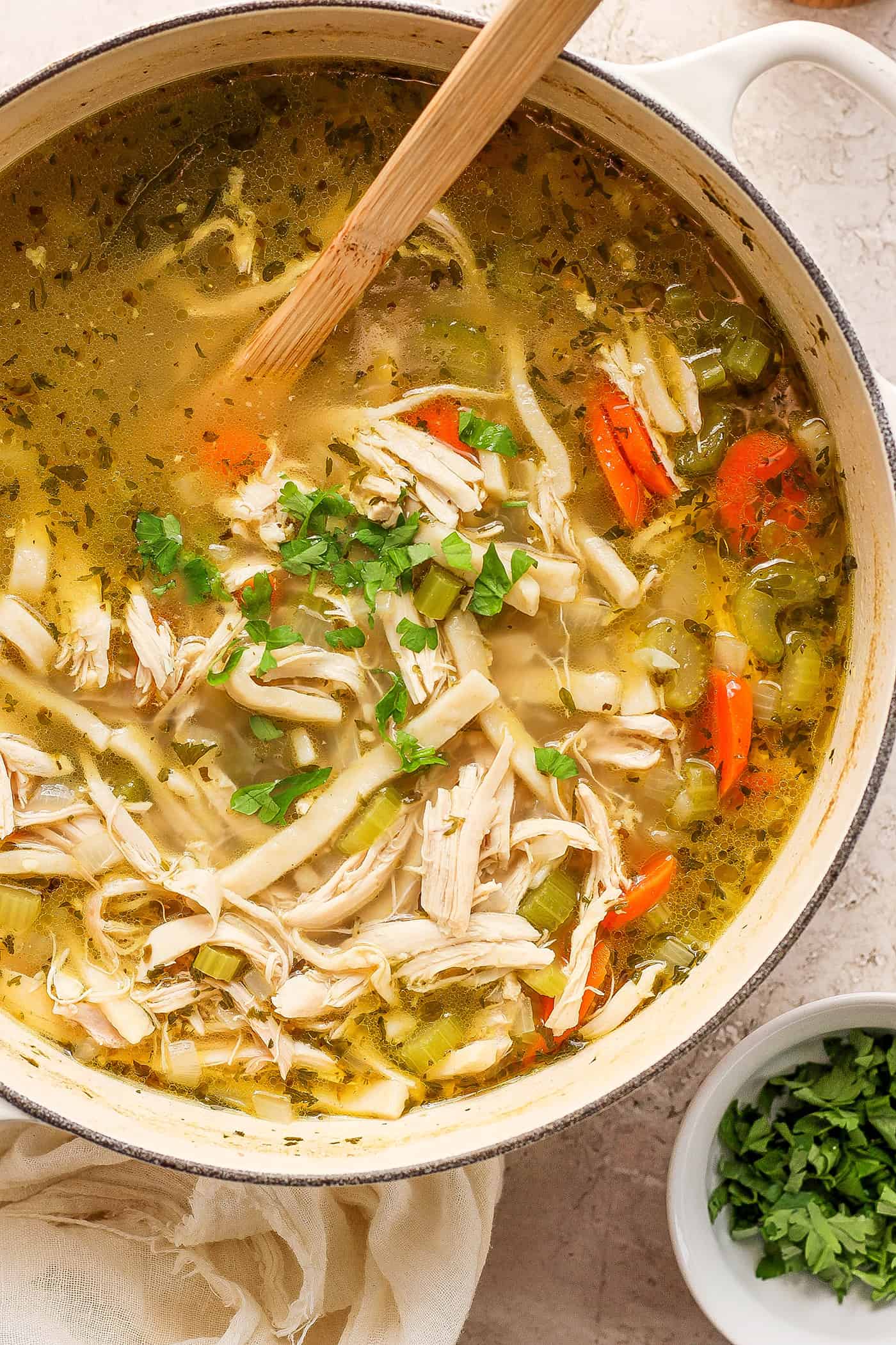 This homemade Chicken Noodle Soup is an easy classic with from-scratch chicken broth loaded with tender chicken, vegetables, and egg noodles. Shredded chicken, herbs and carrots are shown being stirred in a pot of chicken noodle soup.