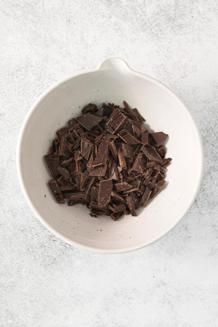 This easy Chocolate Ganache recipe is a versatile staple, perfect for so many things – from cakes to tart fillings to drizzling over coffee! A white bowl full of chopped chocolate.