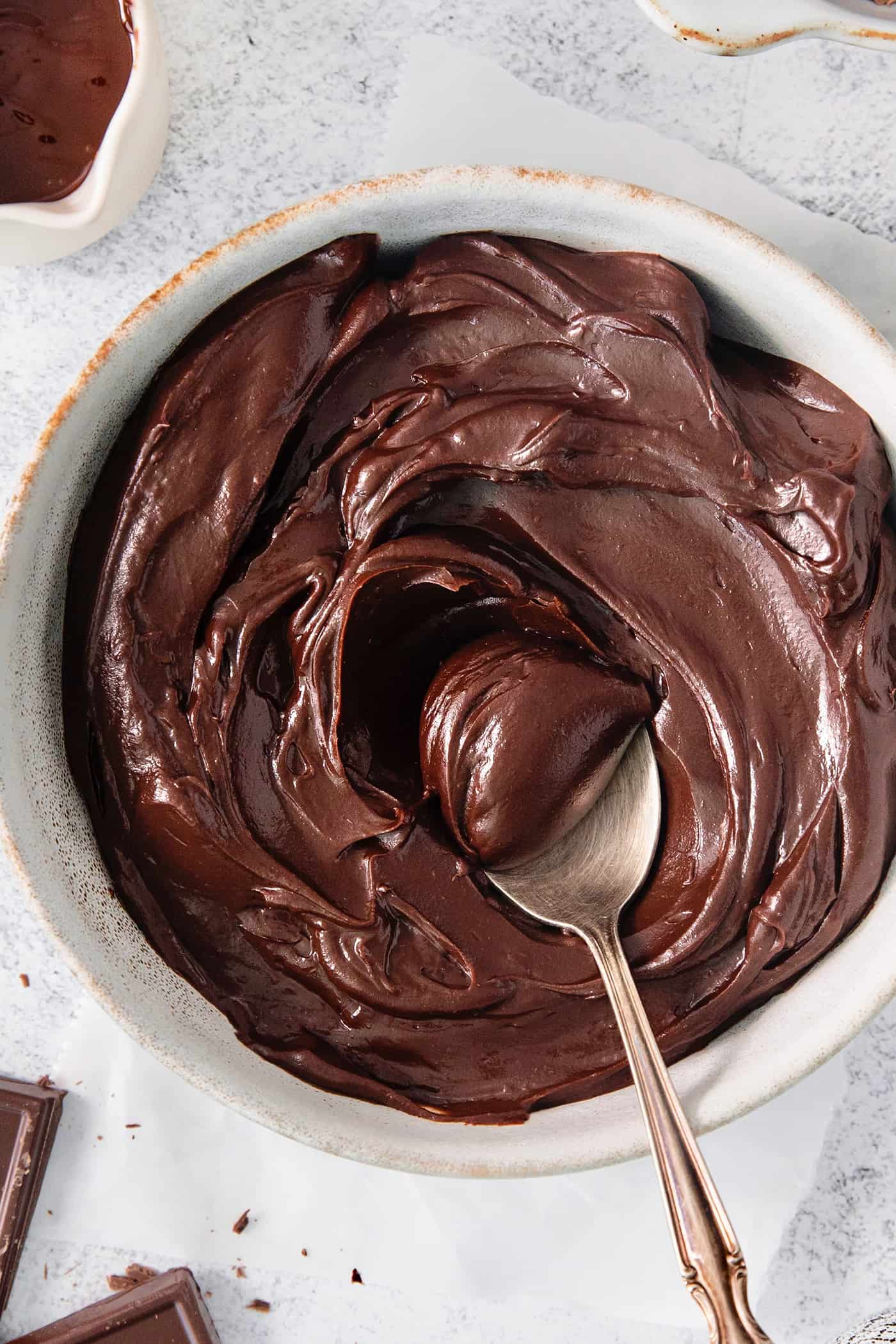 This easy Chocolate Ganache recipe is a versatile staple, perfect for so many things – from cakes to tart fillings to drizzling over coffee! A spoon stirs a bowl of chocolate ganache.