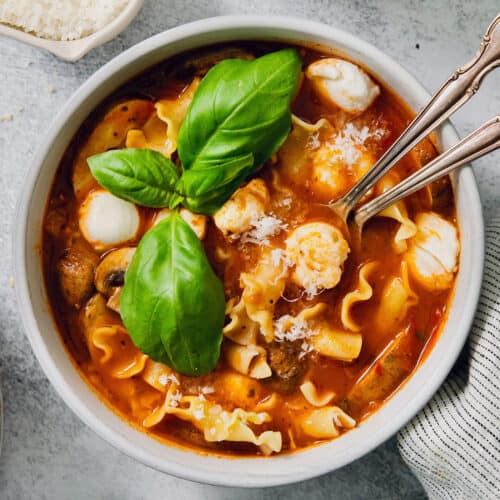 Fresh basil leaves garnish a bowl of slow cooker lasagna soup with chicken.