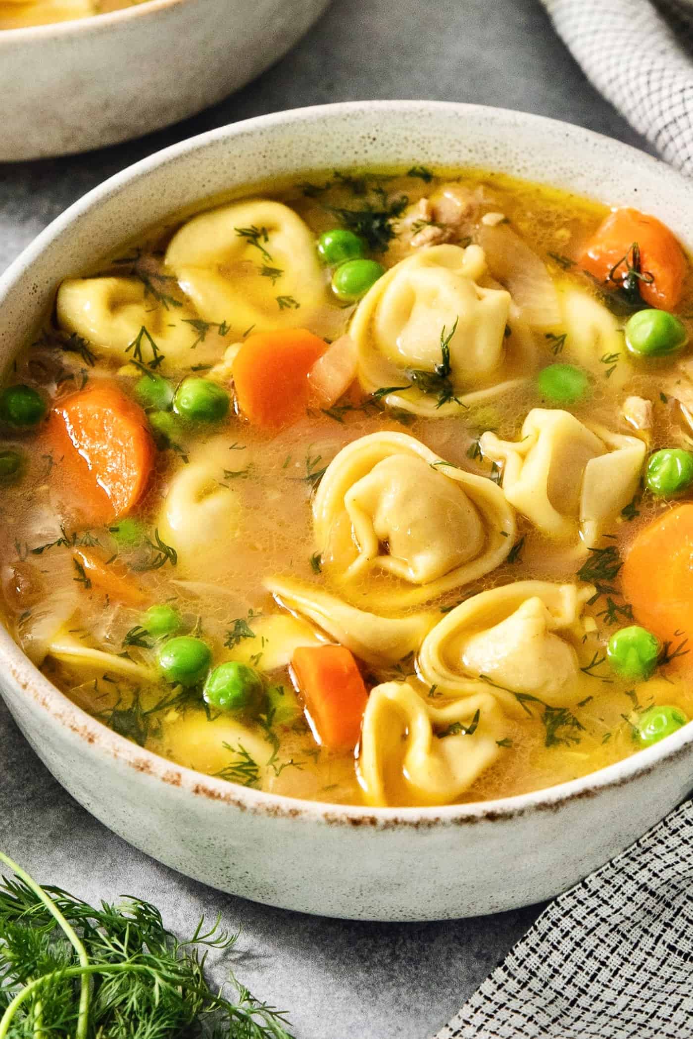 Cheesy tortellini pockets are the stars of this Lemon Chicken Tortellini Soup that also features a lemony broth packed with shredded chicken. A bowl of lemon chicken tortellini soup showing peas, carrots, and torellini.