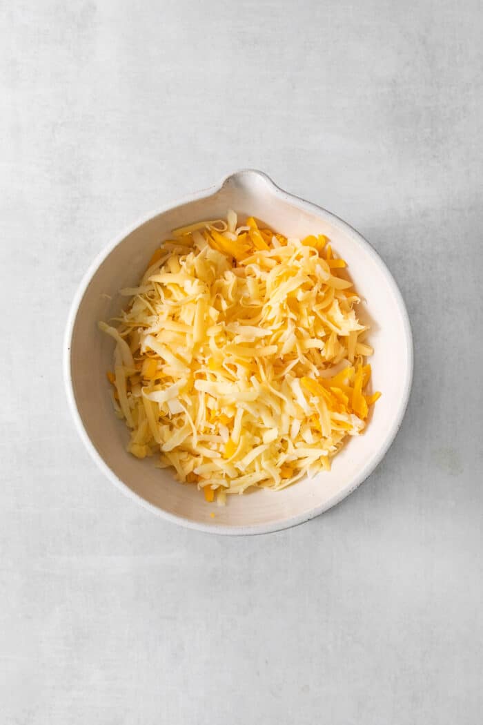 This easy Pulled Pork Mac and Cheese is super decadent with rich and creamy 3-cheese macaroni and cheese plus tender shredded pork. Shredded gouda, fontina, and cheddar cheeses in a white bowl.