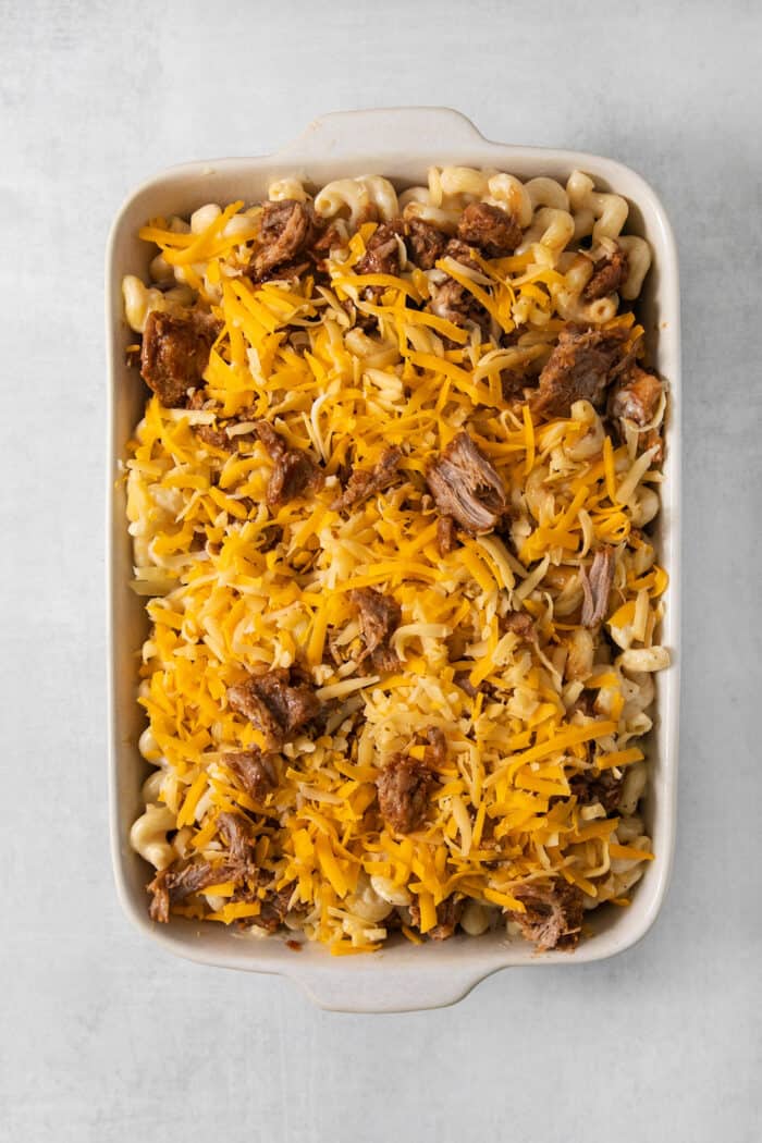 This easy Pulled Pork Mac and Cheese is super decadent with rich and creamy 3-cheese macaroni and cheese plus tender shredded pork. A cheese-topped casserole dish of pulled pork mac and cheese before going in the oven.