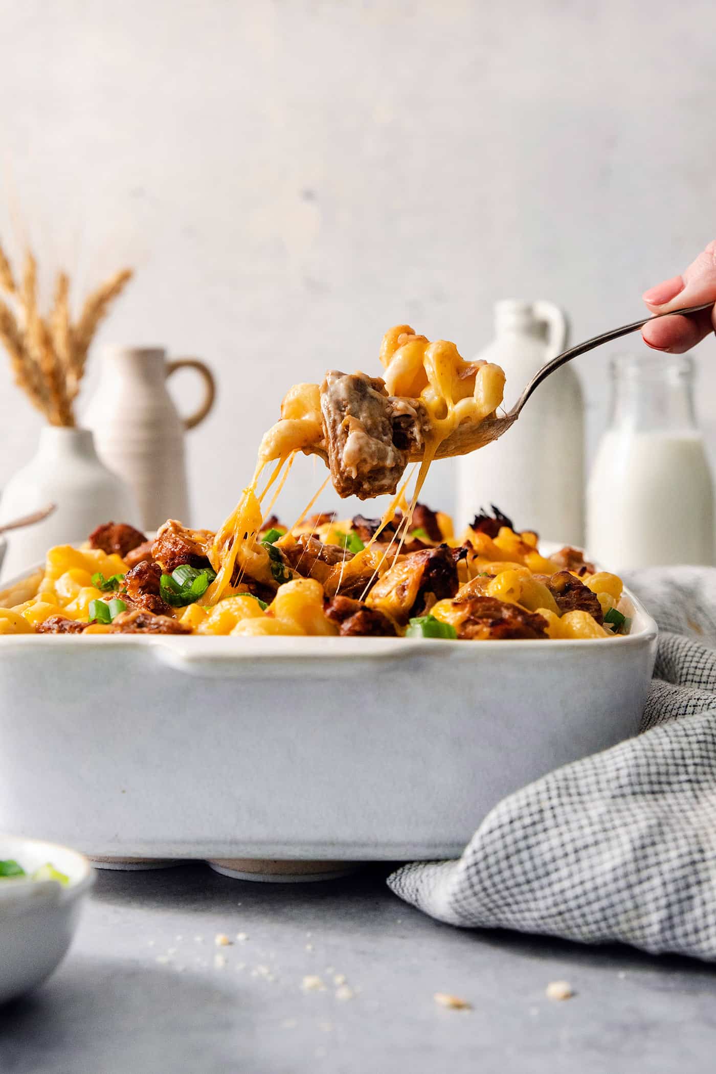This easy Pulled Pork Mac and Cheese is super decadent with rich and creamy 3-cheese macaroni and cheese plus tender shredded pork. A hand lifts a serving spoon of pulled pork mac and cheese from a casserole dish.