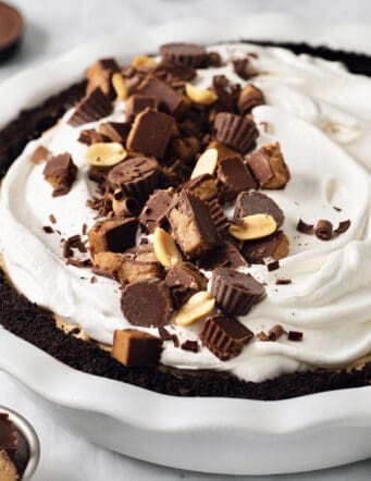 A Reeses pie is shown with half of it topped with chopped peanut butter cups.