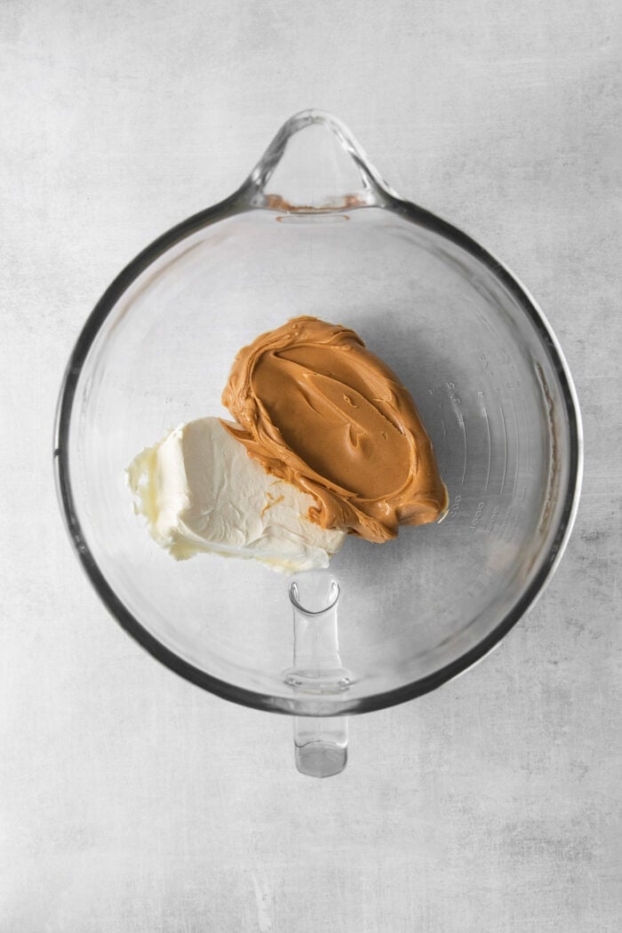 This no-bake Reese’s Pie features a crisp Oreo crust and a creamy peanut butter filling finished with whipped topping and Reese’s cups. Cream cheese and peanut butter are added to a glass bowl.