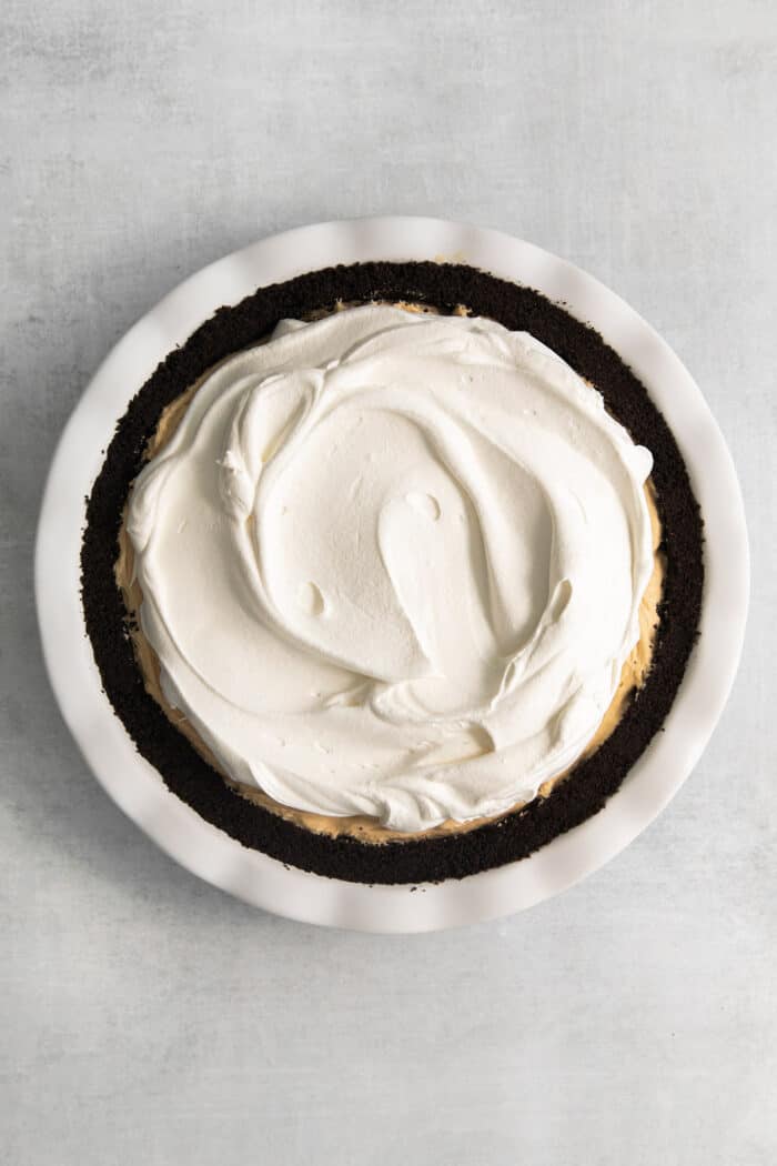 This no-bake Reese’s Pie features a crisp Oreo crust and a creamy peanut butter filling finished with whipped topping and Reese’s cups. Whipped topping is spread across the surface of the pie.