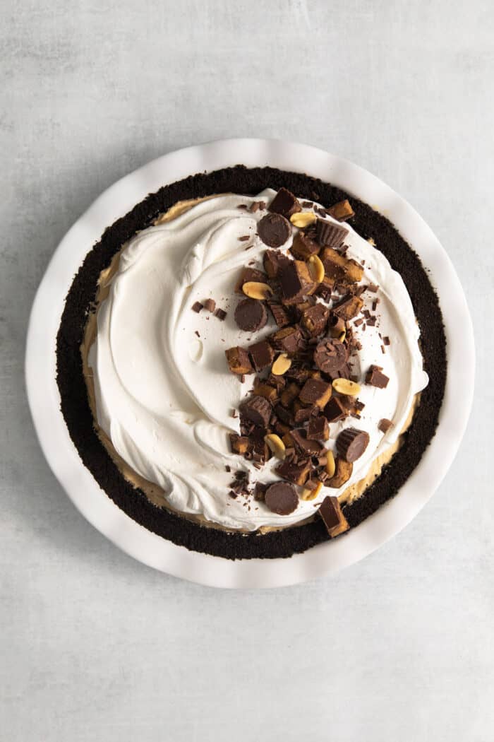 This no-bake Reese’s Pie features a crisp Oreo crust and a creamy peanut butter filling finished with whipped topping and Reese’s cups. The pie is topped with chopped peanut butter cups.