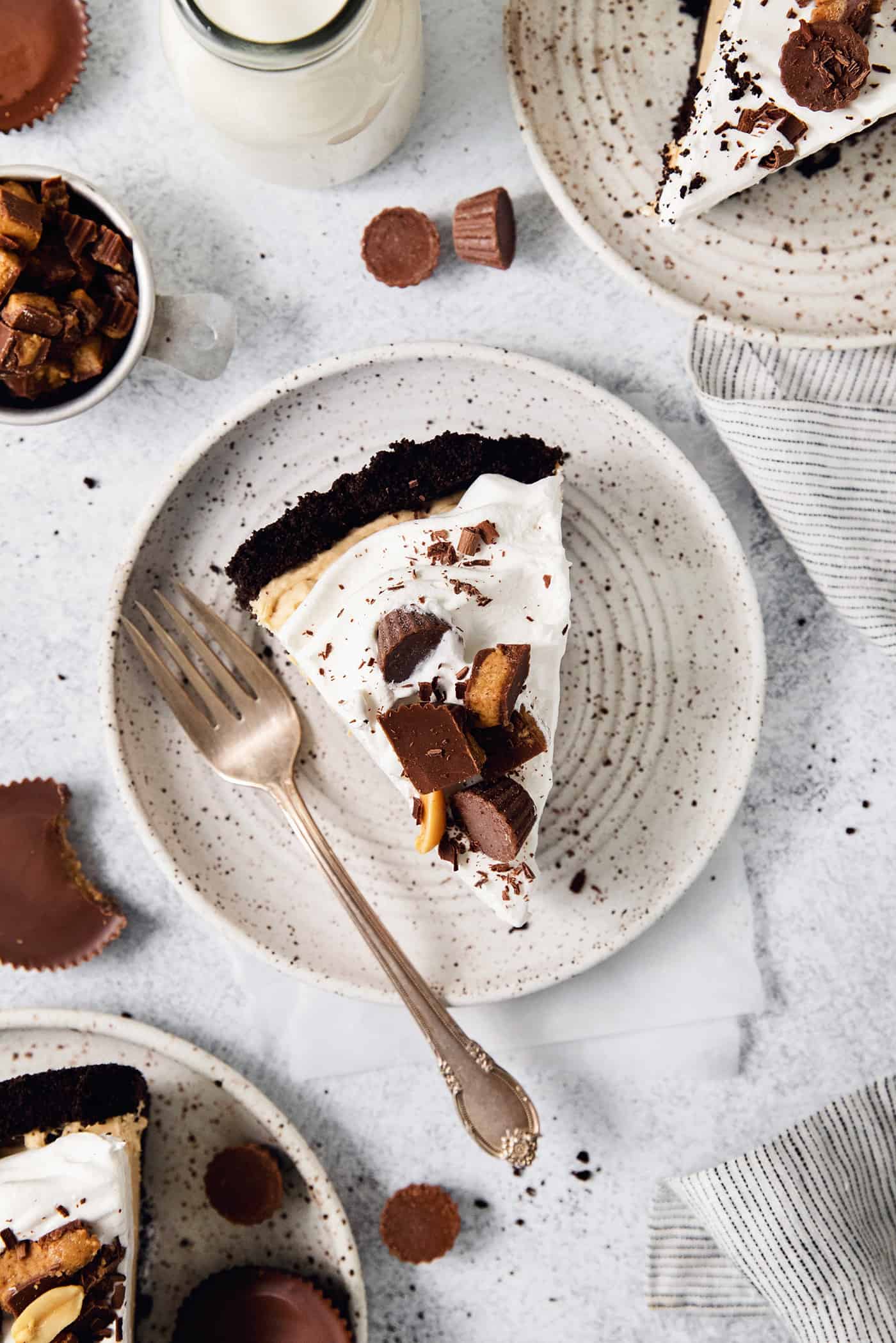 This no-bake Reese’s Pie features a crisp Oreo crust and a creamy peanut butter filling finished with whipped topping and Reese’s cups. A slice of Reeses pie on a plate with a fork, topped with chopped peanut butter cups.
