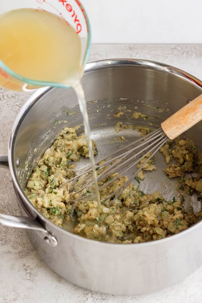 Broth is whisked into the vegetables in the soup pot.