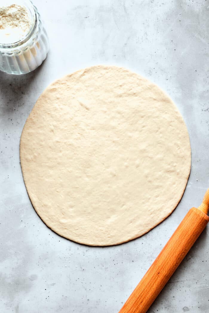 This Cheeseburger Pizza recipe turns your favorite burger into pizza! Top homemade dough with pizza sauce, ground beef, cheese, and pickles. A circle of pizza dough is rolled out.