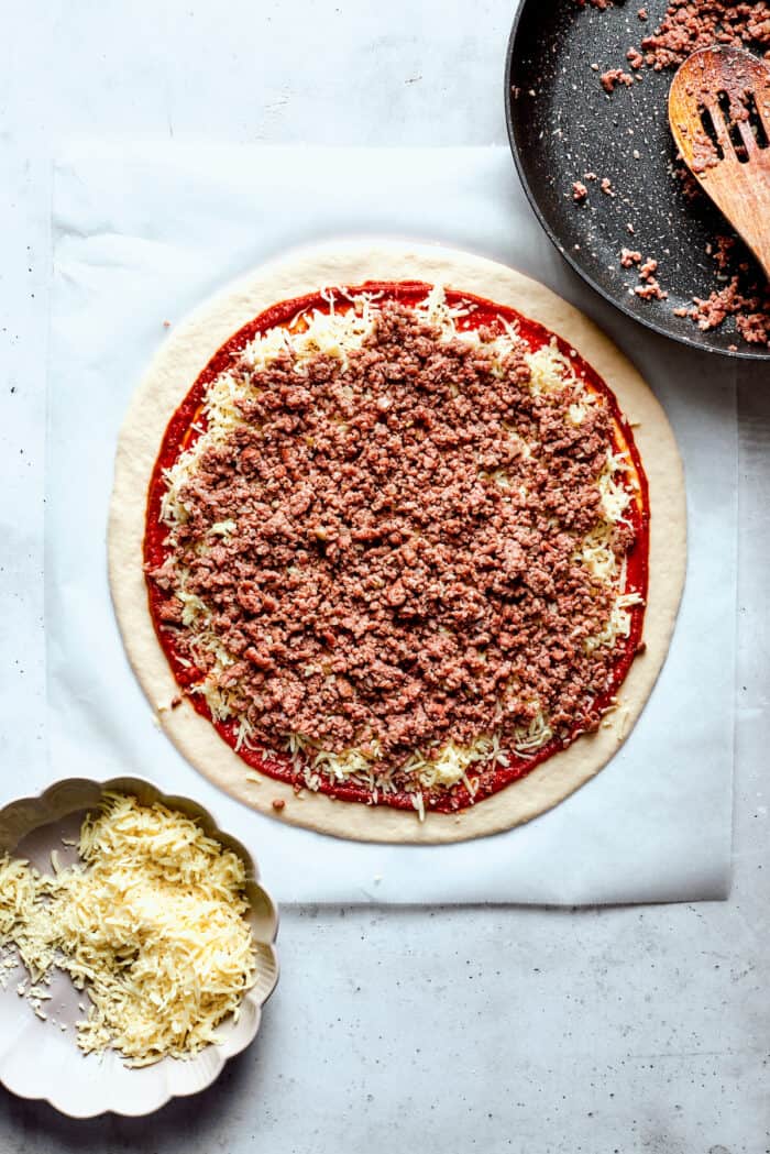 This Cheeseburger Pizza recipe turns your favorite burger into pizza! Top homemade dough with pizza sauce, ground beef, cheese, and pickles. The cooked meat is added to the pizza.