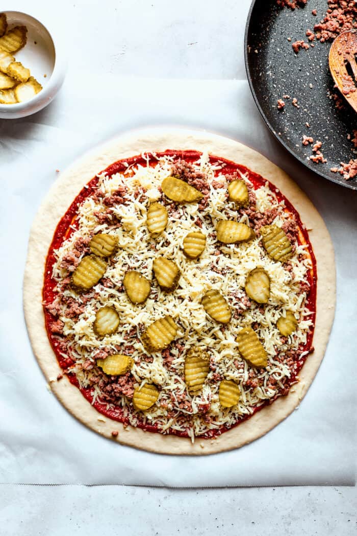 This Cheeseburger Pizza recipe turns your favorite burger into pizza! Top homemade dough with pizza sauce, ground beef, cheese, and pickles. Pickles are added to the pizza.