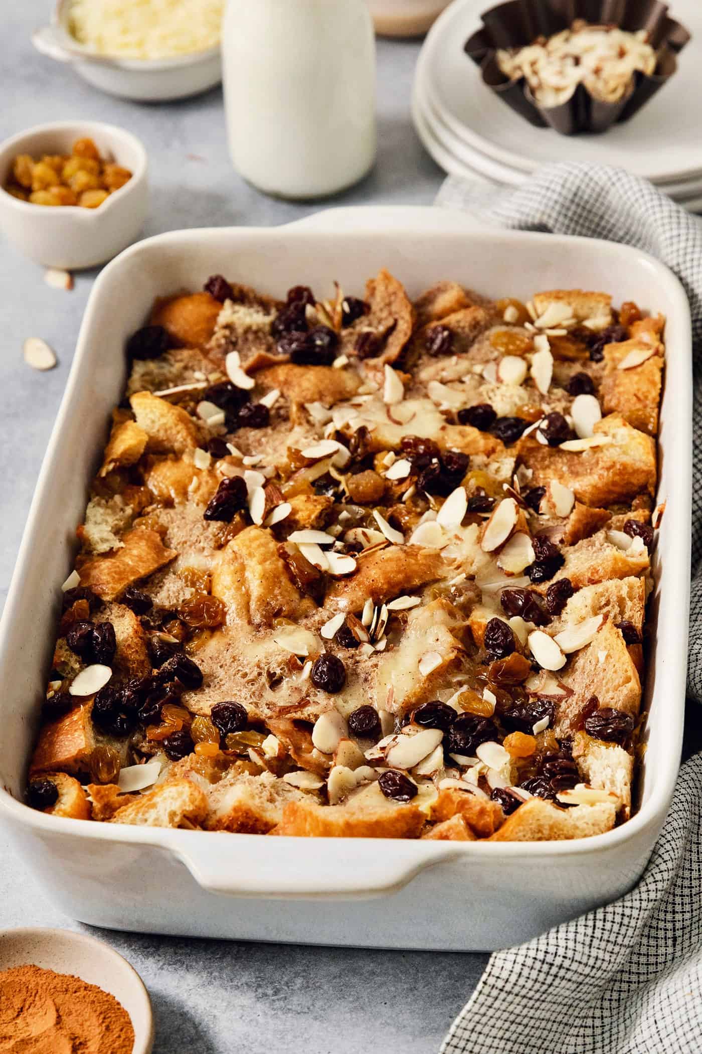 Capirotada, or Mexican Bread Pudding, features layers of crusty bread, raisins, sliced almonds, and cheese soaked in spiced sweet cream. A baking dish full of capirotada topped with raisins and almonds.