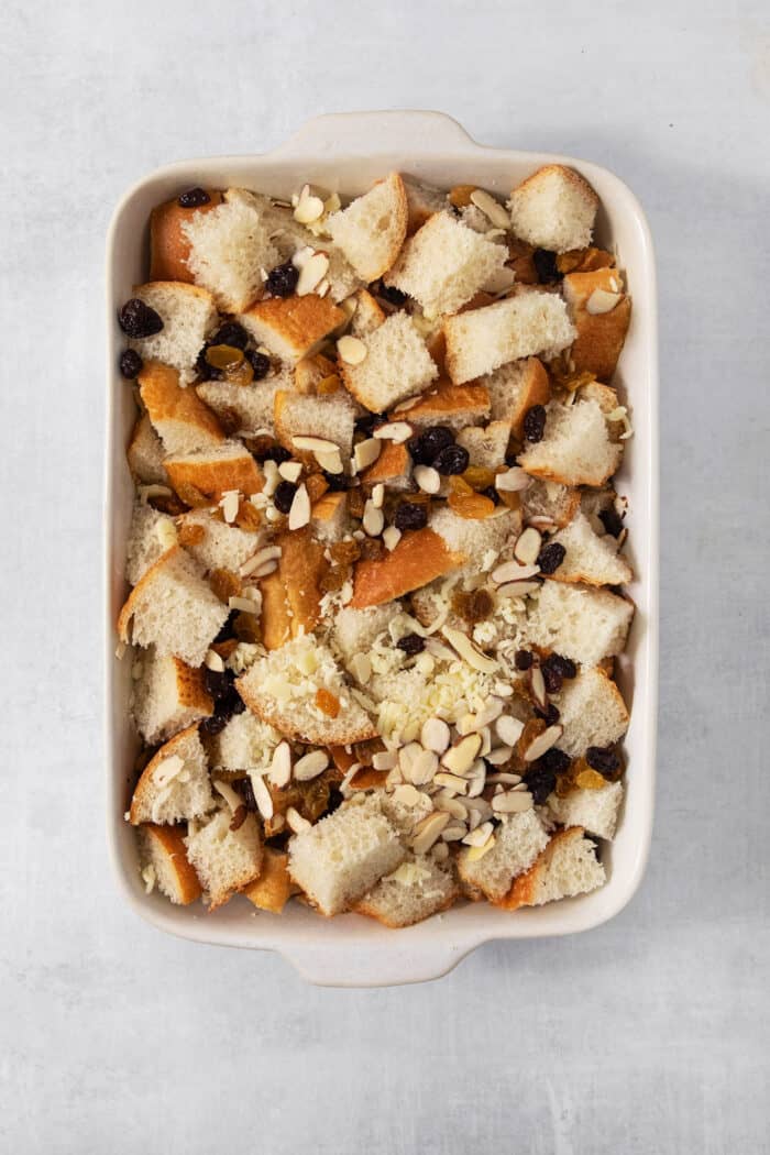Capirotada, or Mexican Bread Pudding, features layers of crusty bread, raisins, sliced almonds, and cheese soaked in spiced sweet cream. Shredded rolls, cheese, raisins, and almonds are combined in a baking dish.