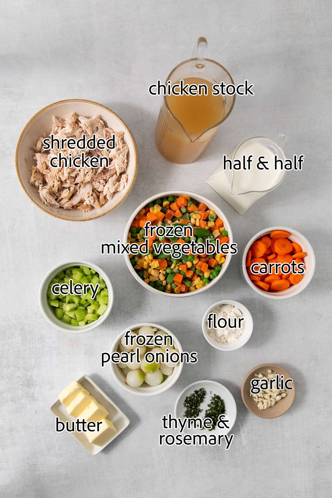 This homemade Chicken Pot Pie Soup recipe features a creamy broth that’s loaded with chicken and vegetables and topped with biscuits. Chicken pot pie soup ingredients are shown portioned out: carrots, celery, chicken, flour, half and half, broth, frozen onions, frozen vegetables, salt, garlic, butter.